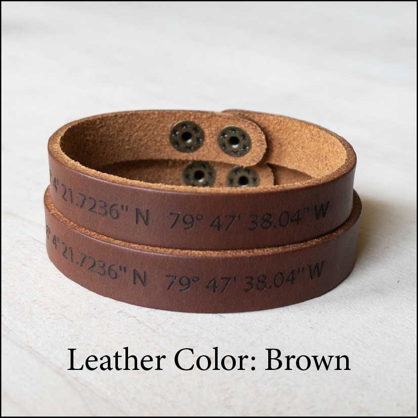 a set of two matching couples bracelets engraved with custom navigation coordinates. The bracelets are made with brown leather and brass snaps.